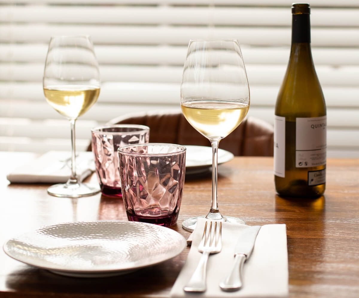 A bottle and two glasses of white wine on a dinner table with water glasses, plate and cutlery