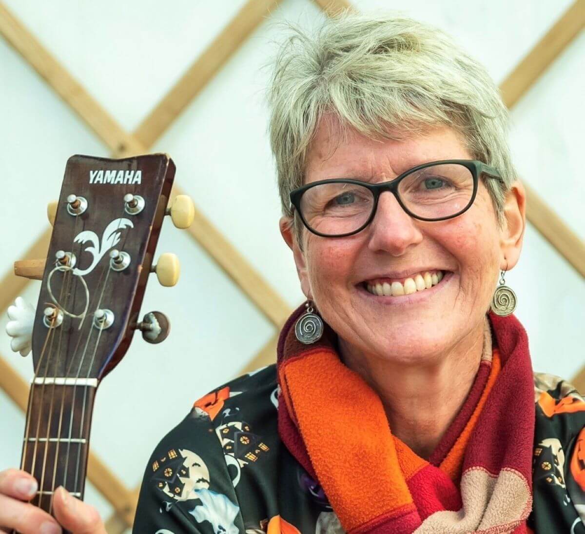 A person smiles and holds up a guitar