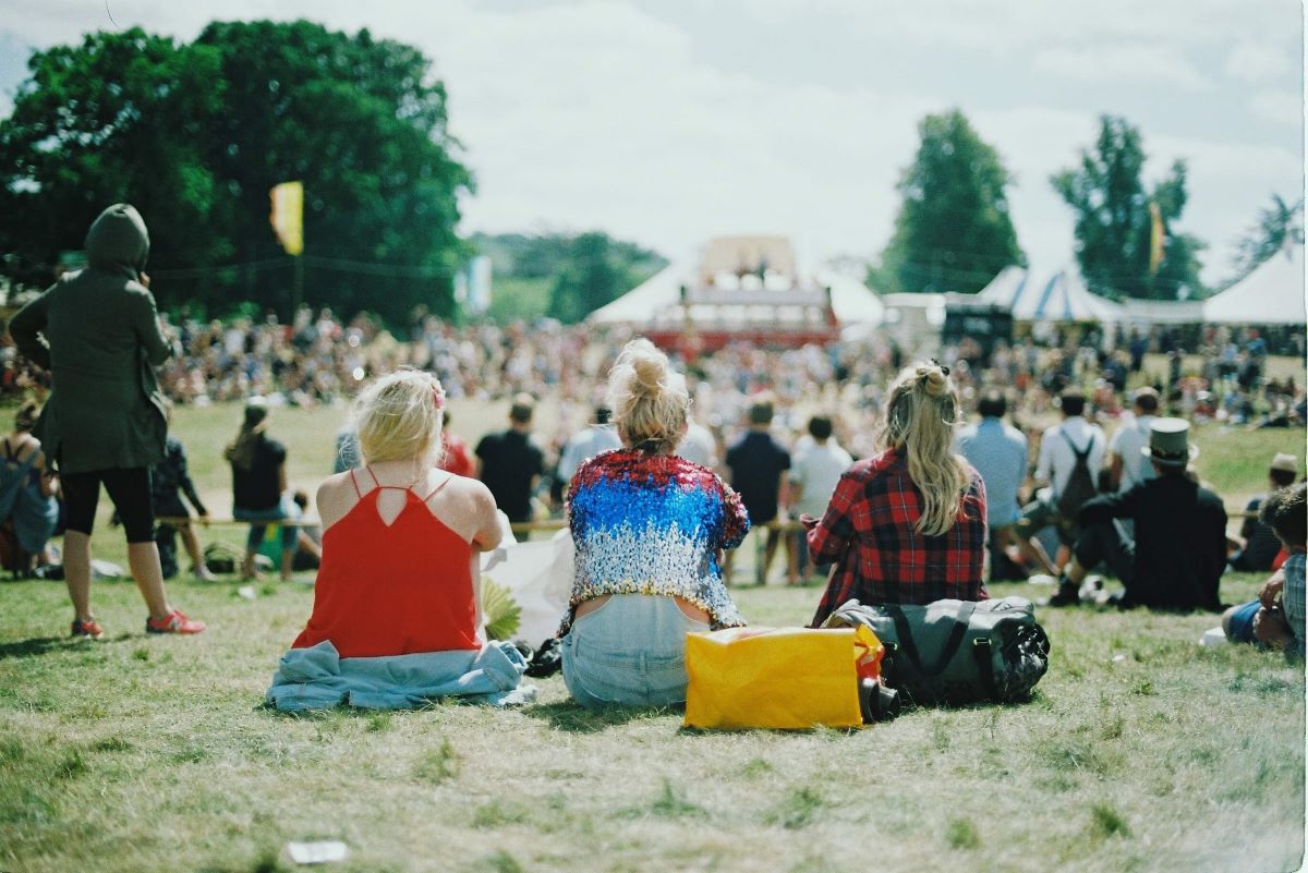 Three people sat on the grass at a music festival