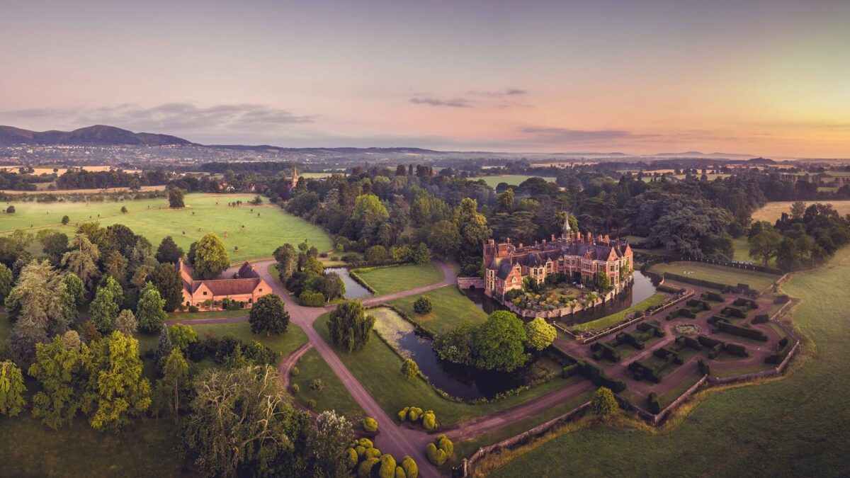 An aerial view of Madresfield Court with surrounding moat and gardens and Malvern Hills in background