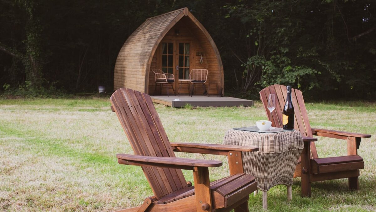 A wooden glamping pod with two outdoor chairs and a table placed on grass outside