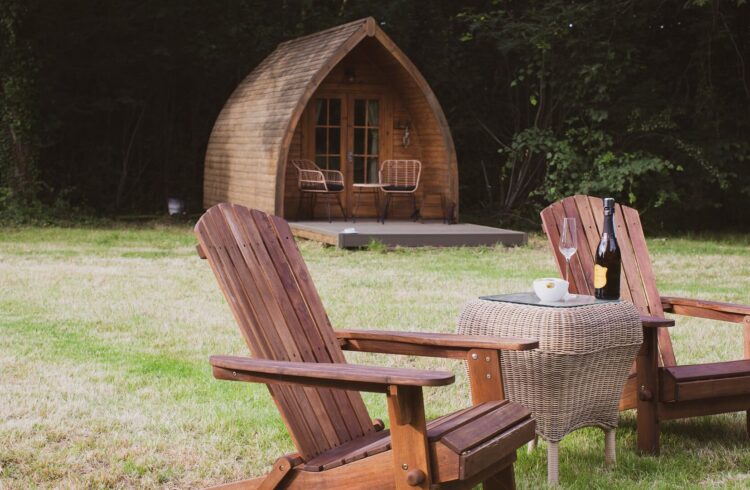 A wooden glamping pod with two outdoor chairs and a table placed on grass outside