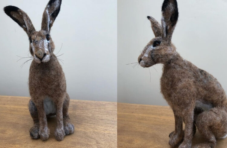 A needle felted hare displayed on a wooden table against a grey background