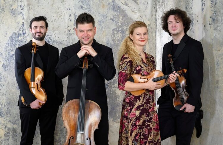 All four members of the Pavel Haas Quartet dressed for a concert and standing facing the camera