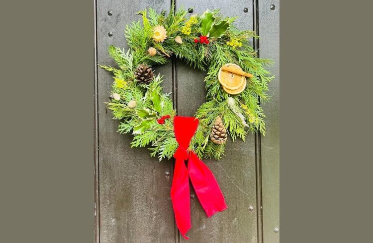 A Christmas wreath featuring foliage, cones, holly on a green door