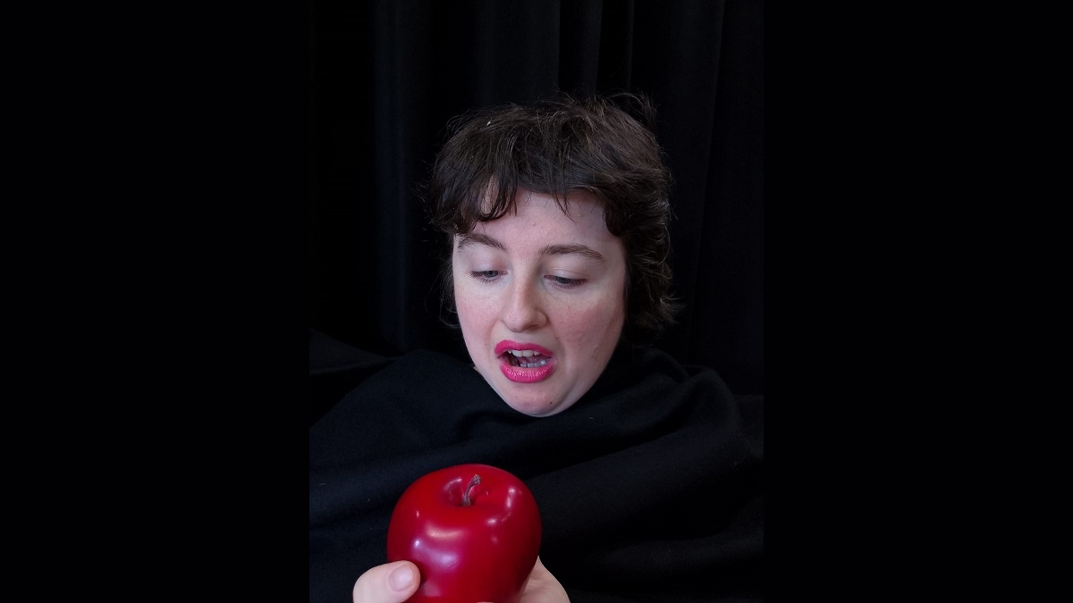 A woman, dressed in black, looking at a red apple