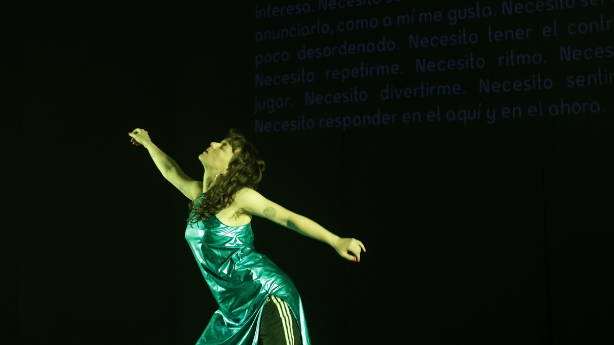 A person wearing a shiny green dress with arms outstretched in opposite directions