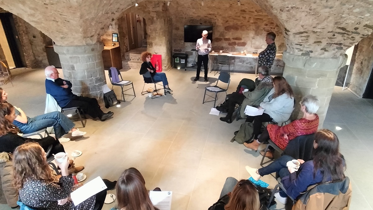 A group of people seated in a crypt, listening to a talk